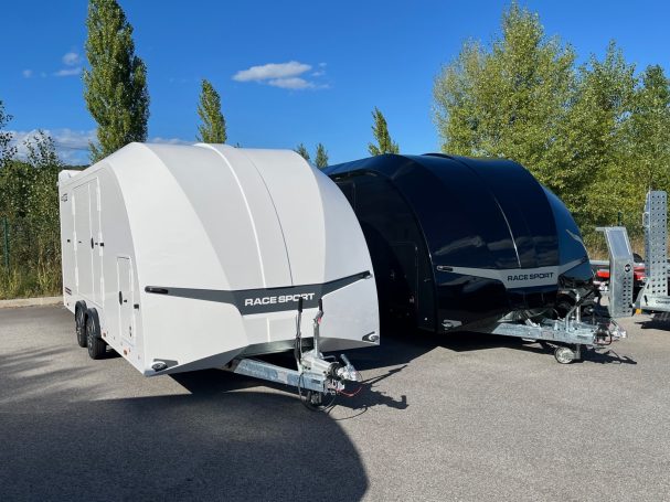 Deux caravanes de camping, une blanche et une noire, stationnées sous un ciel bleu.